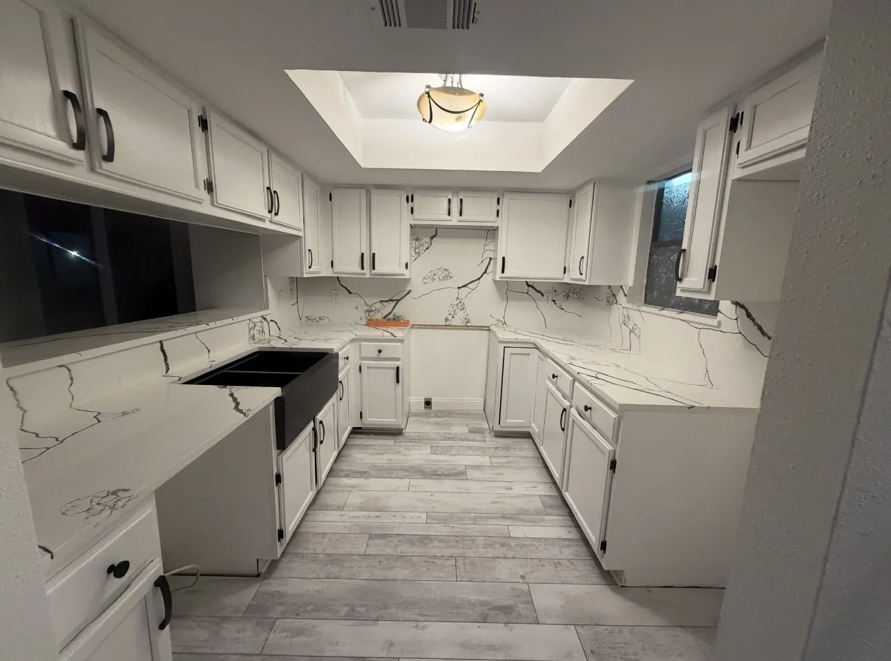 Galley kitchen after cabinet painting, white cabinets with black hardware against a marbled backsplash and a farmhouse sink
