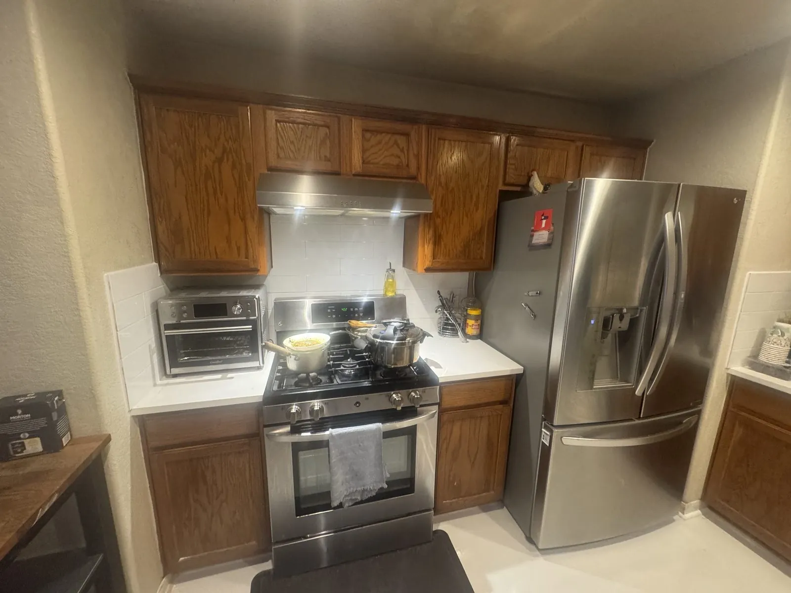 Kitchen before painting, honey oak cabinets around a stainless range and hood with a white tile backsplash