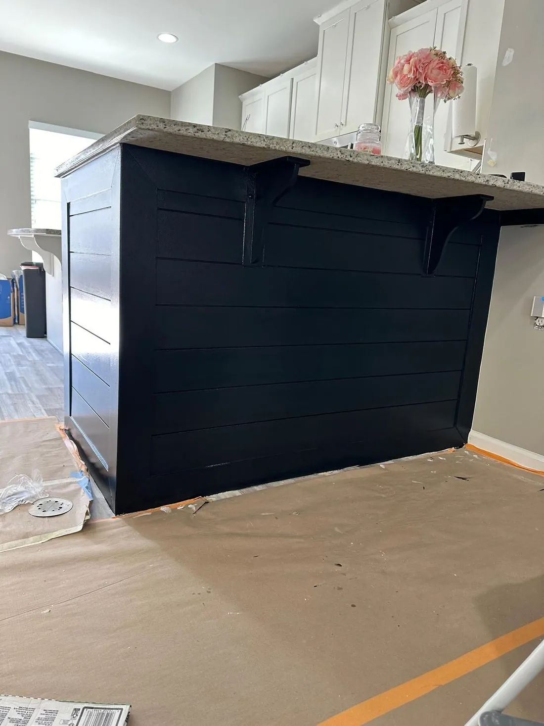 The same kitchen peninsula after painting, the shiplap and corbels finished in deep navy against the granite bar top