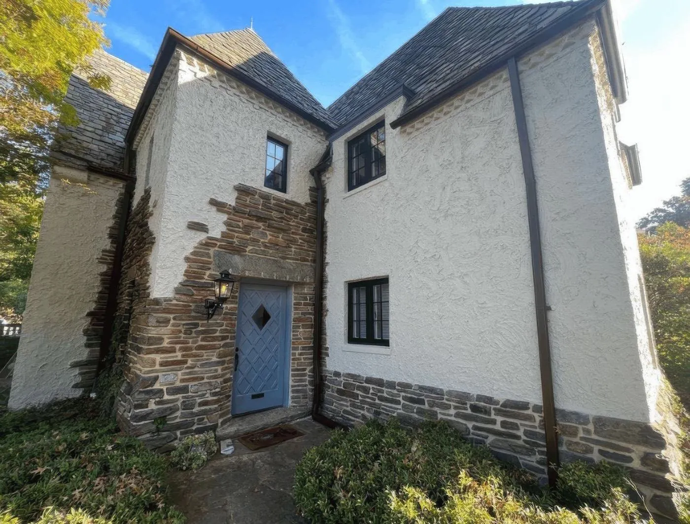 Stucco and fieldstone two-story home after a full exterior repaint by Rise and Prime Painting, with a blue-gray lattice front door