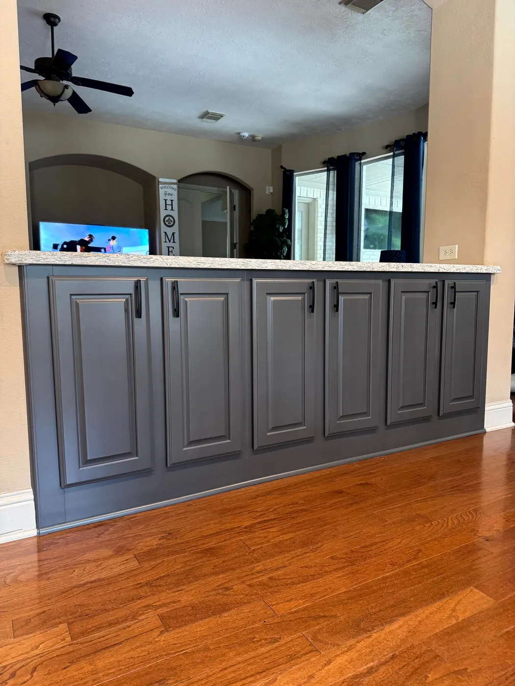 Back of a kitchen peninsula with raised-panel cabinet doors painted slate gray, above an oak hardwood floor