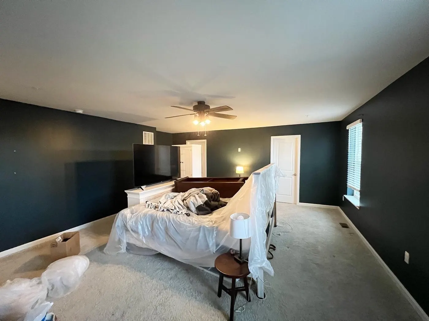 Bedroom walls painted charcoal, the bed and furniture wrapped in plastic mid-job