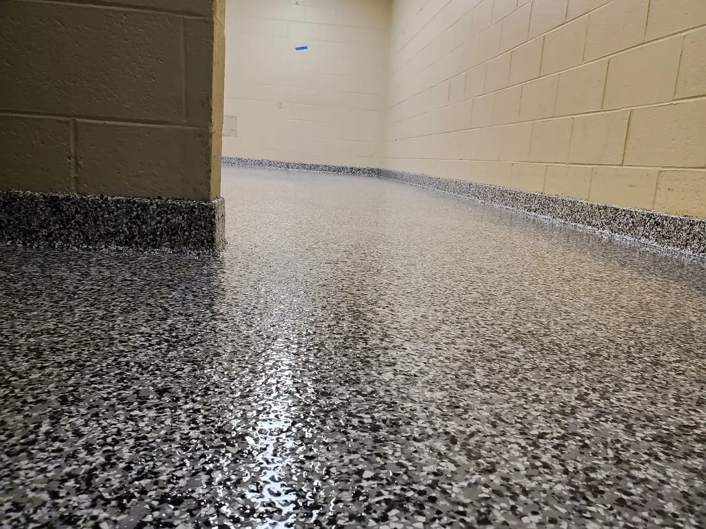 Close view of a gray and black flake floor coating where it meets a painted block wall