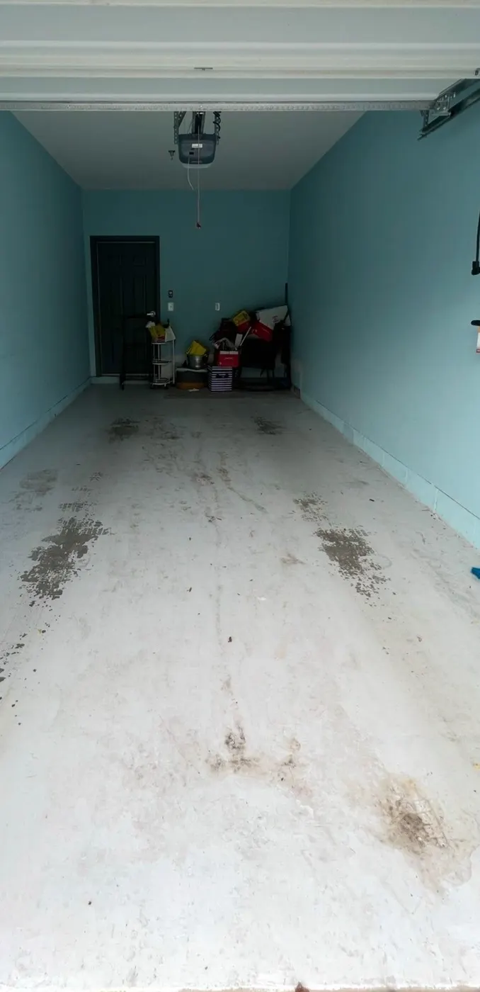 Long narrow garage before the floor coating, the bare concrete worn and stained, walls painted turquoise and a black door at the far end