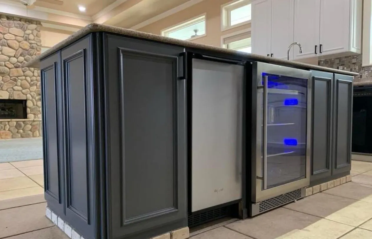 The same kitchen island after painting, the cabinet panels finished in charcoal gray around the beverage fridge and dishwasher