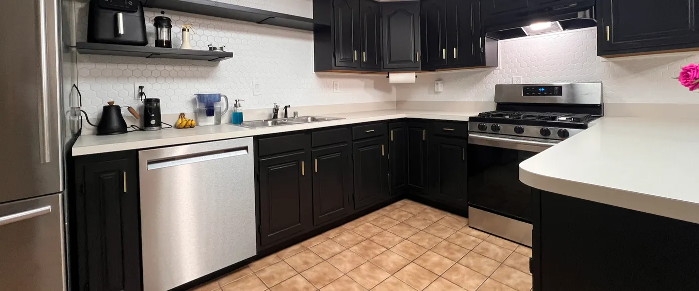 Kitchen cabinets painted black above and below white counters, a white hexagon tile backsplash, floating shelves and a stainless range