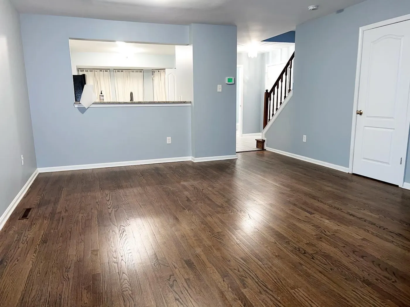 Living room painted pale blue with white trim and a pass-through window to the kitchen, over a hardwood floor
