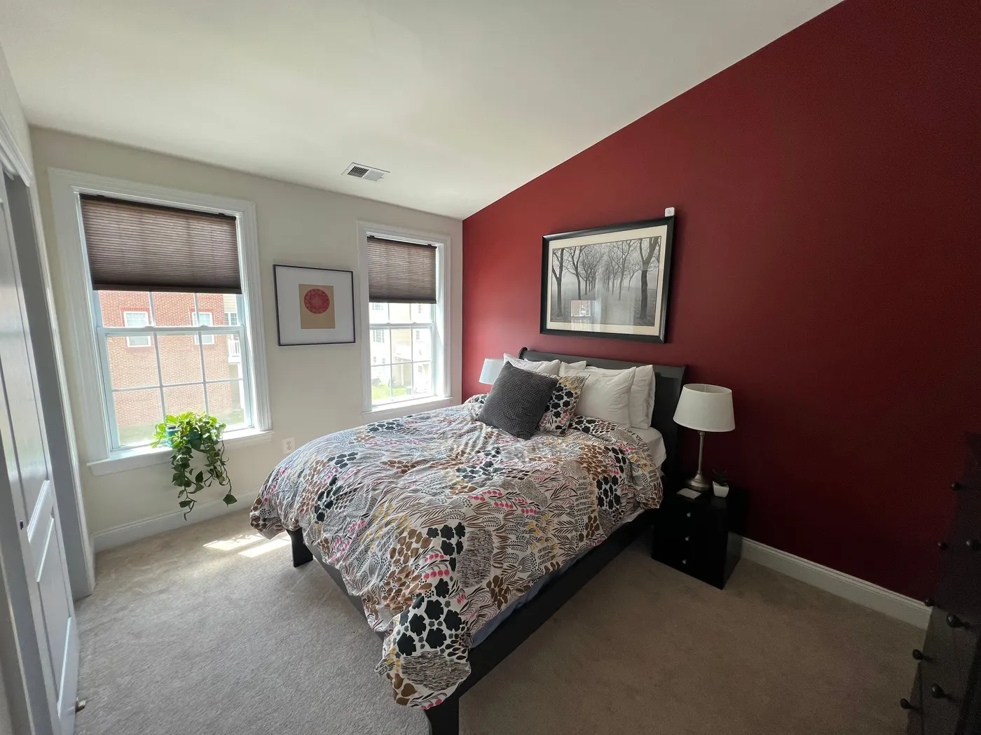 Bedroom with a deep red accent wall behind the bed, beside two windows with white trim