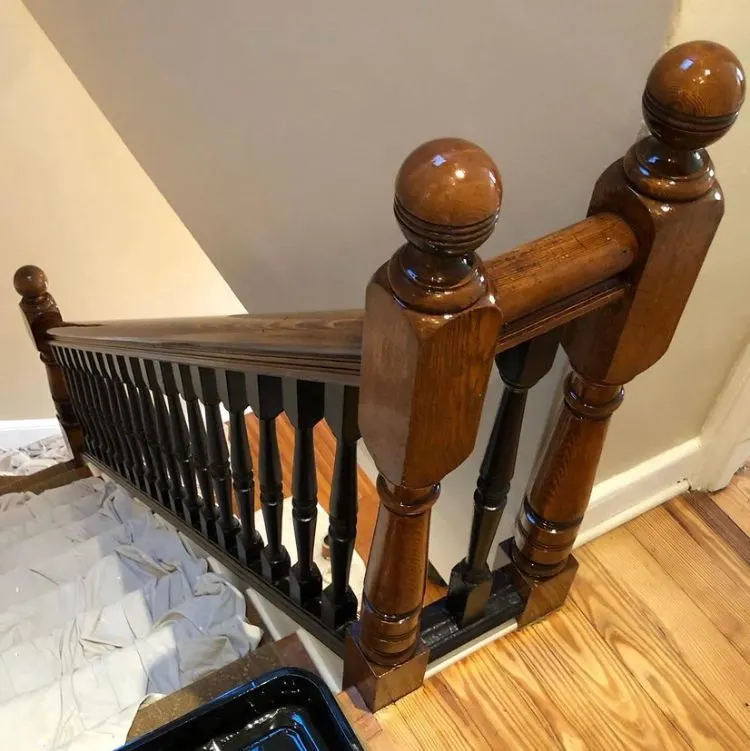 Stained wood newel posts and handrail over black painted balusters, a drop cloth on the treads below