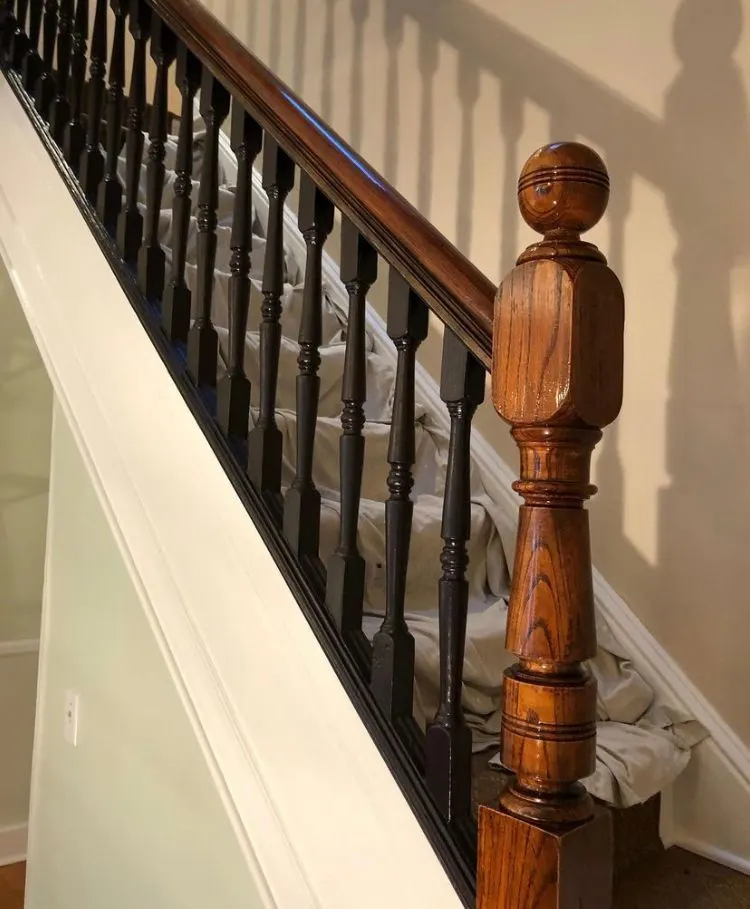 Staircase with a stained handrail and turned newel post over black painted balusters, against a white wall