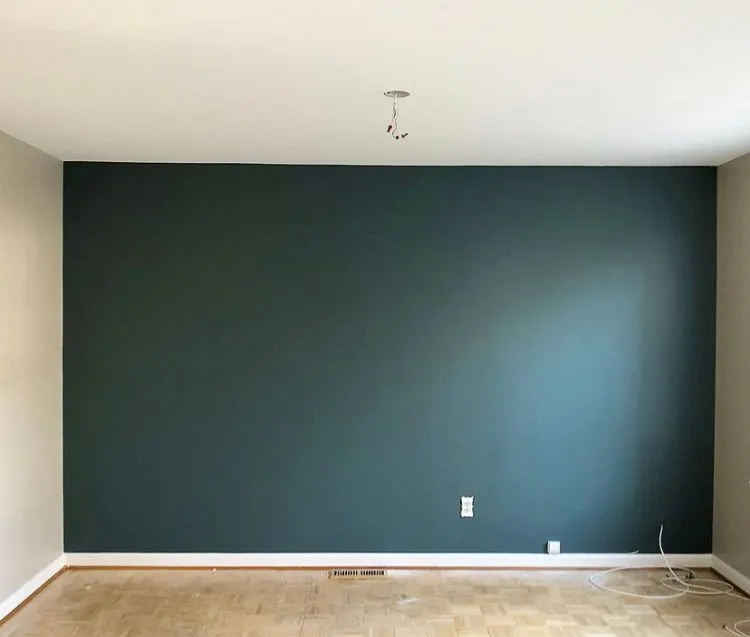 Empty room with a dark teal accent wall and white side walls above a parquet wood floor