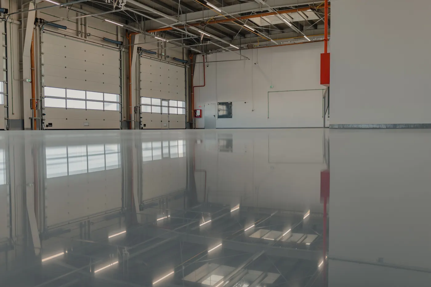 Warehouse floor coated in high-gloss gray, reflecting the loading bay doors and the ceiling lights