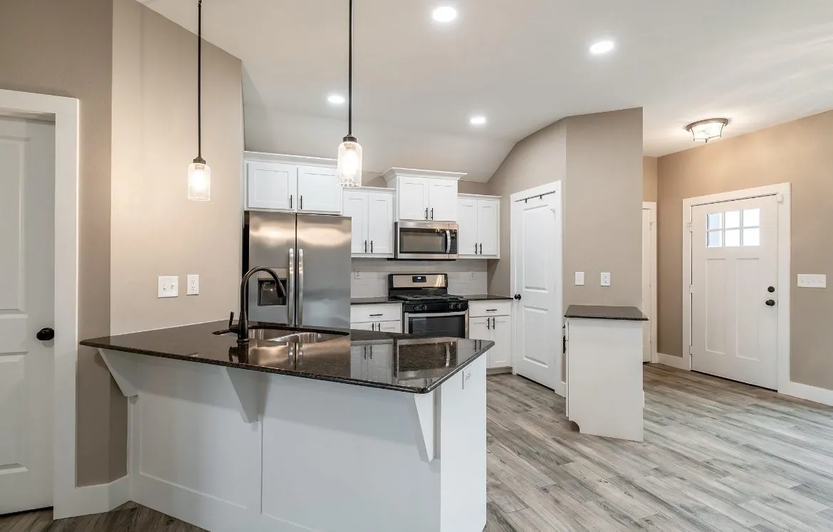 Open plan kitchen and entry after an interior repaint, greige walls with white trim and doors, white cabinets and a dark granite bar top