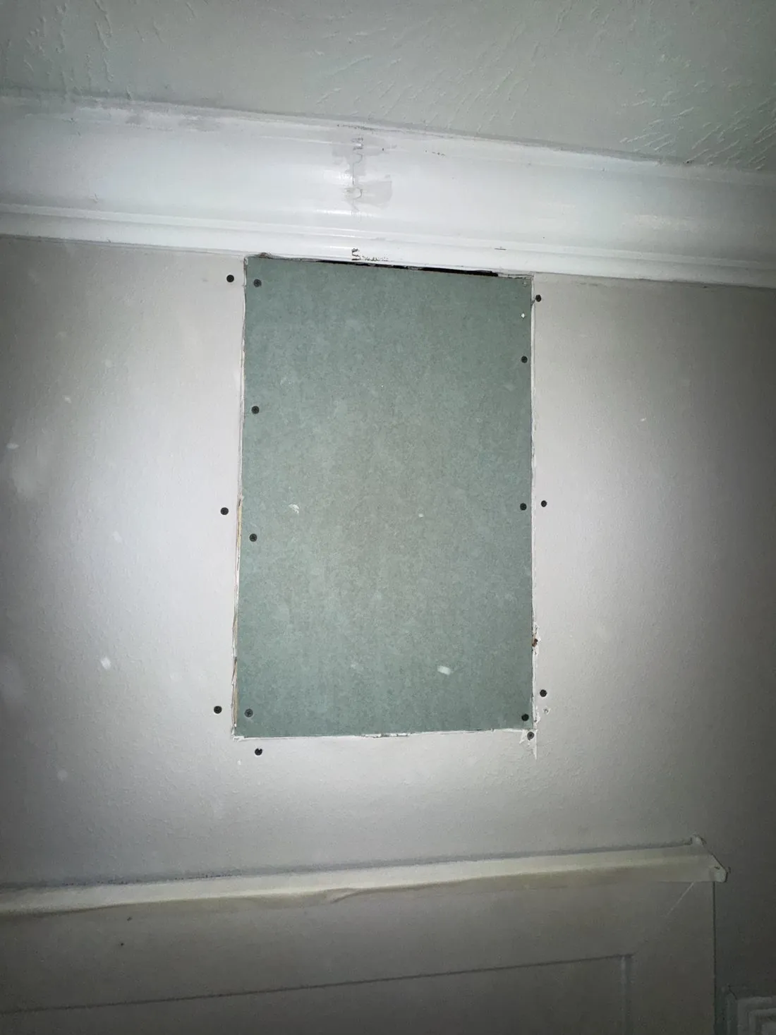 The same wall opening filled with a screwed-in drywall patch, flush with the surrounding wall and ready for tape and compound