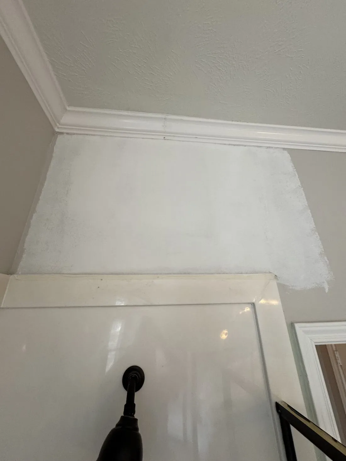 Interior stairwell wall skim coated with fresh compound below the crown molding, the repair feathered out and drying before paint