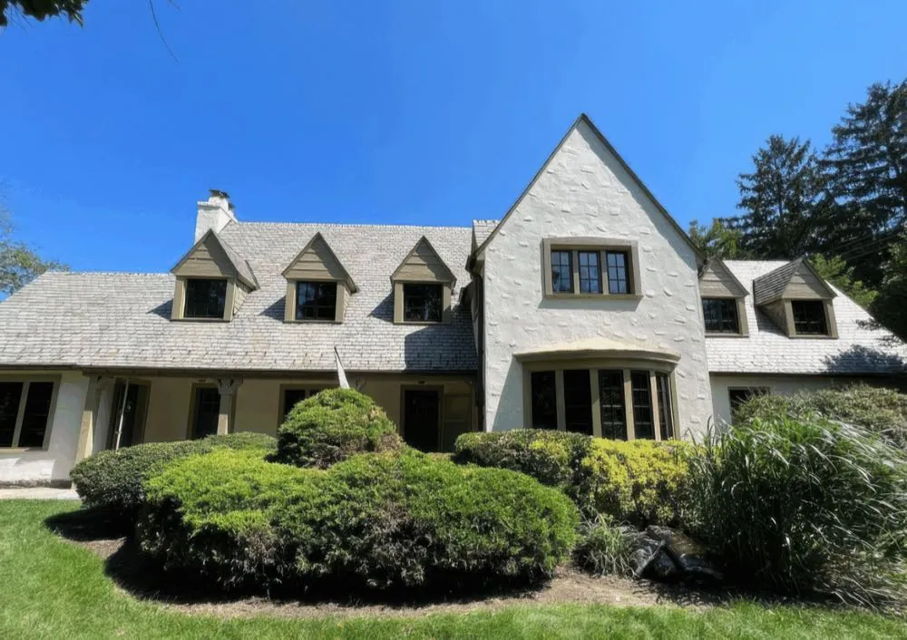 Full front elevation of a stucco home with gabled dormers in a gray shingle roof, after an exterior repaint by Rise and Prime Painting