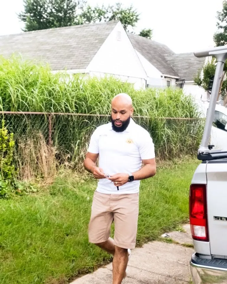 Ray Gomez, owner of Rise and Prime Painting, in a company polo beside a white work truck with a ladder rack