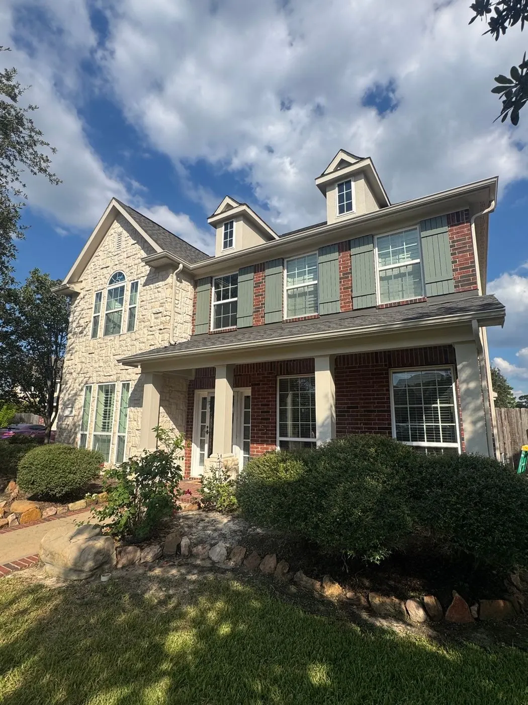 Two-story brick house with a stone front, cream siding upstairs and sage green shutters, after an exterior repaint