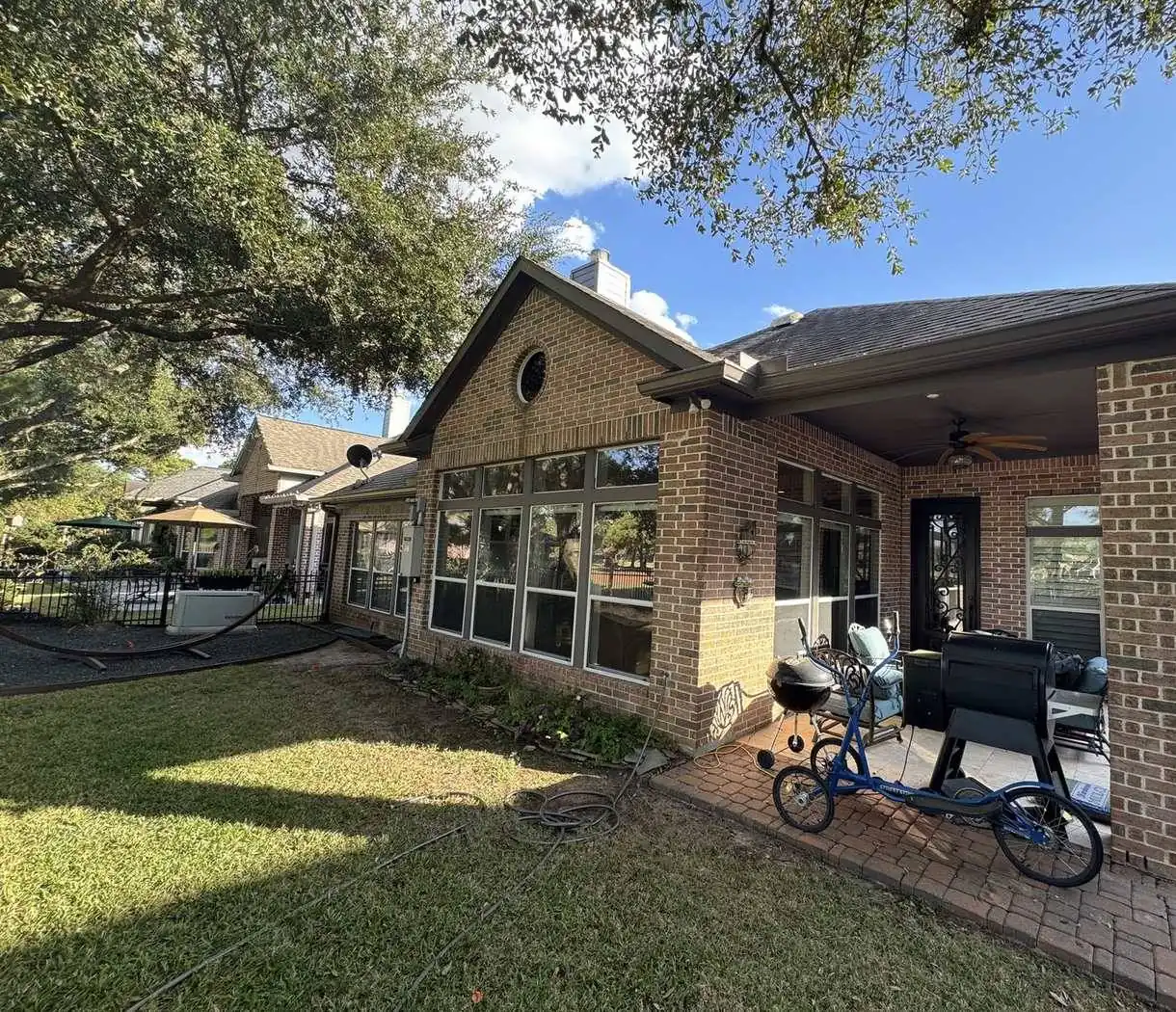 Red brick ranch home with a deep covered patio, the soffit and fascia repainted dark brown, live oaks overhead and a golf course lot behind