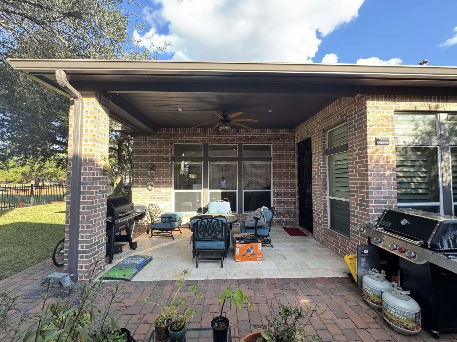 Finished covered patio on a brick home, the beadboard ceiling and beams painted dark brown, patio furniture and a grill back in place on the paver floor