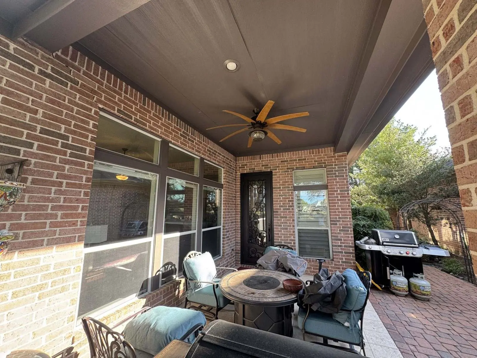 Dark brown painted patio ceiling and ceiling fan on a brick home, looking out past the brick columns to the yard