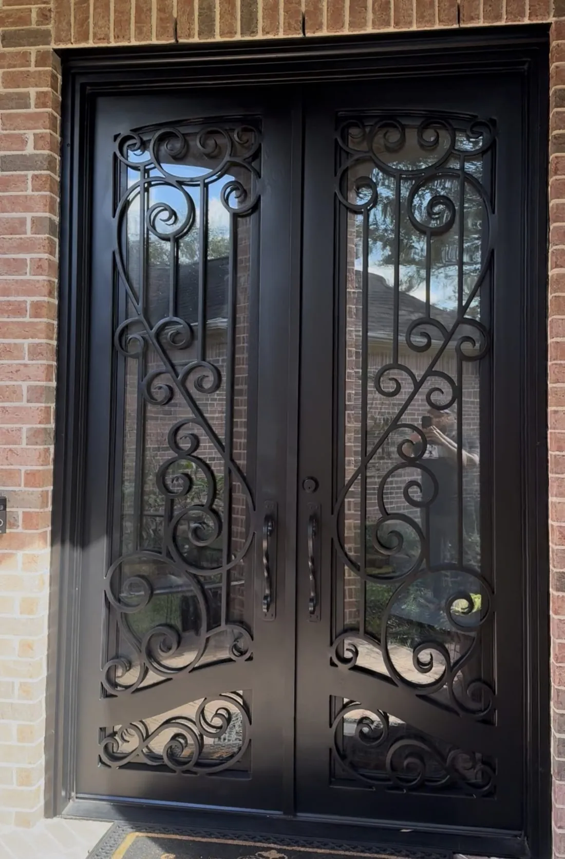 Wrought iron double entry door on a brick home refinished in satin black, the scrollwork and glass panels clean and the brick surround untouched